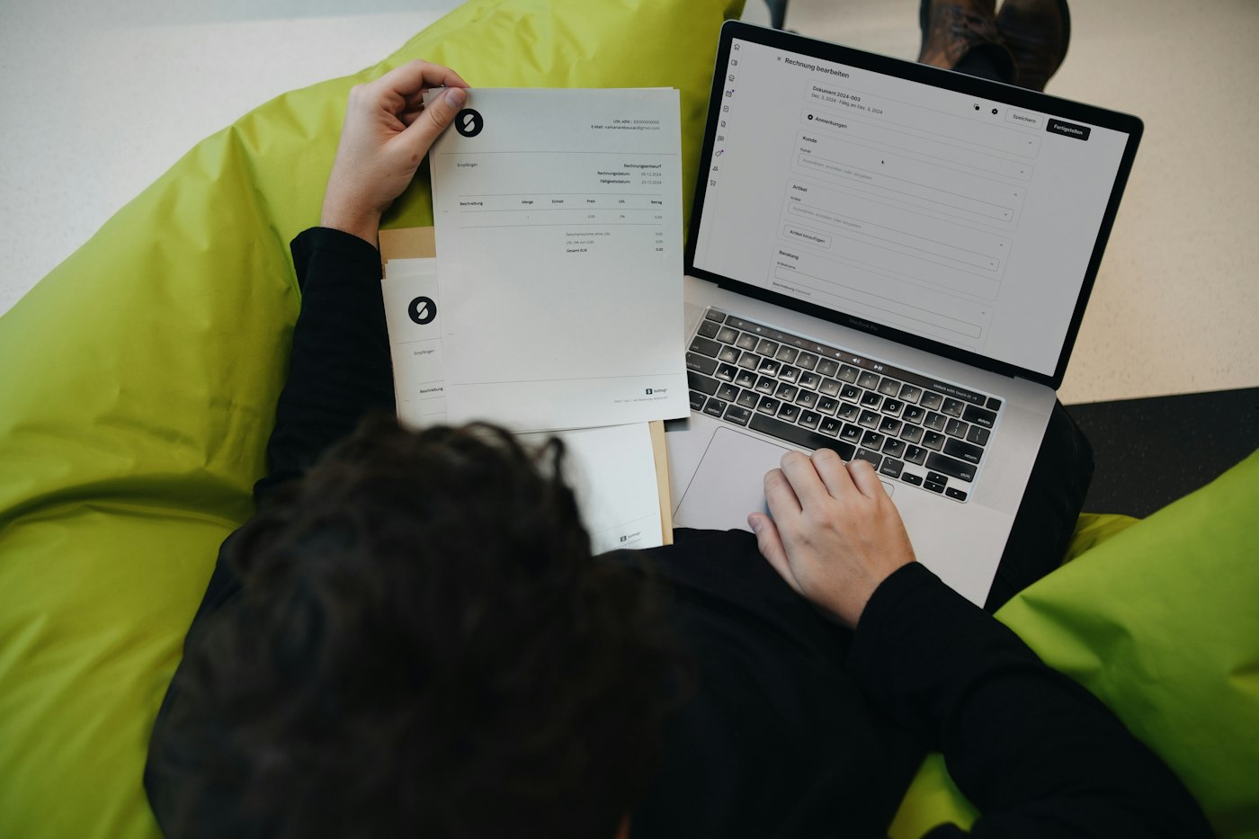 Draufsicht auf eine Person mit ausgedruckter Rechnung und einem Laptop mit geöffnetem Rechnungsformular